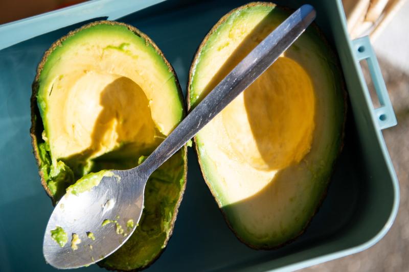 A spoon lies over a sliced avocado.