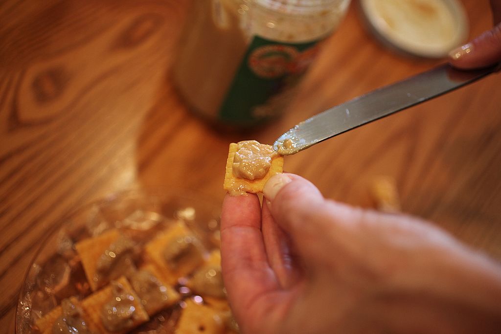 A person spreads nut butter over a cheese cracker