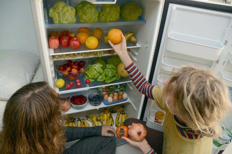 two girls picking out veg from fridge