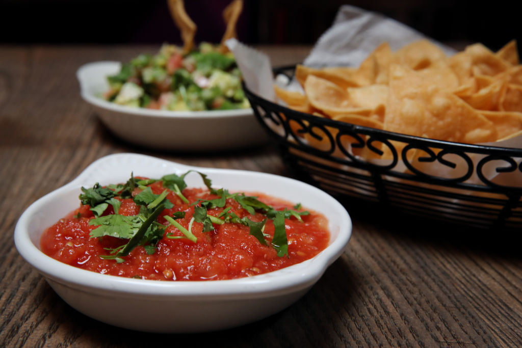 Salsa is pictured in front of chips and a salad.