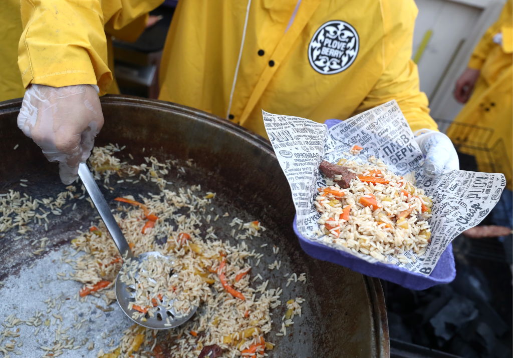 A person scoops a cooked rice dish with a ladle.