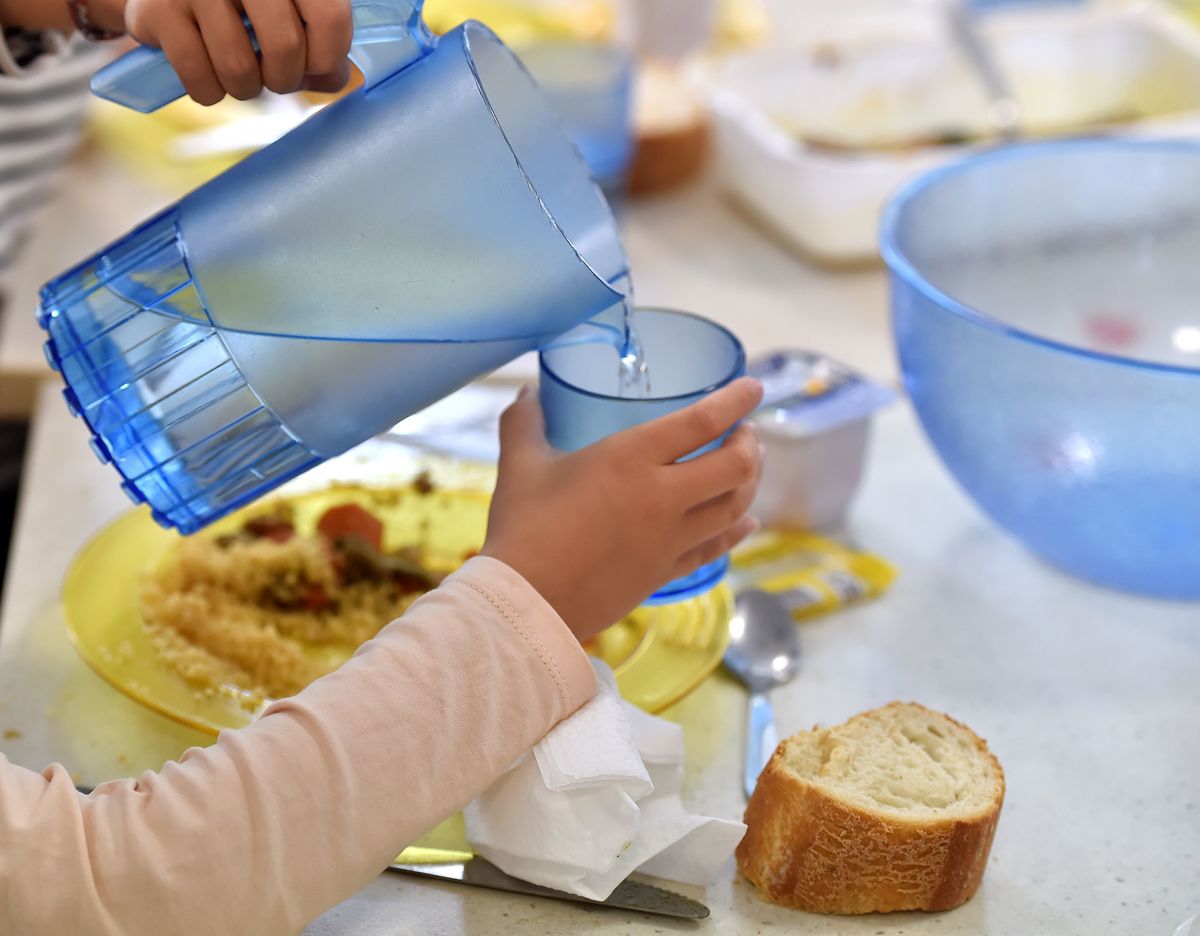 children pouring drinking water from a jug into a plastic beaker while eating lunch