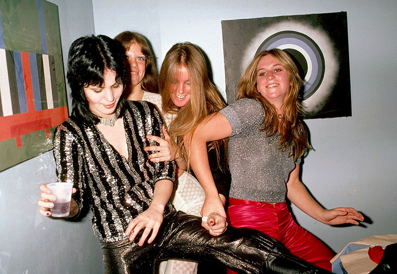 Four members of the runaways fall into one another while smiling backstage.