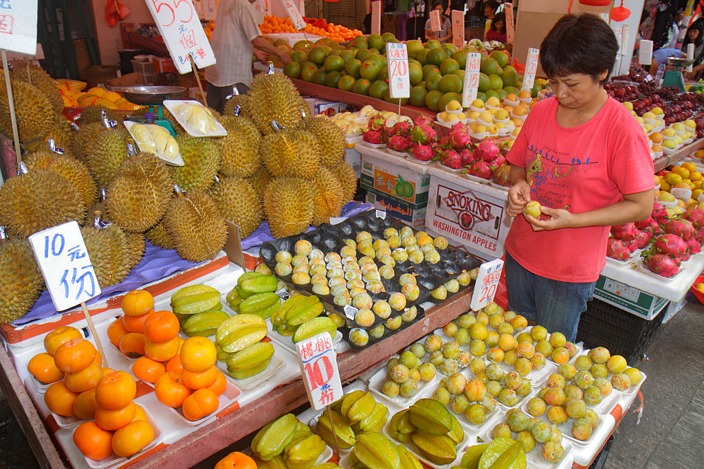 a woman looking at various types of exotic fruit at a market