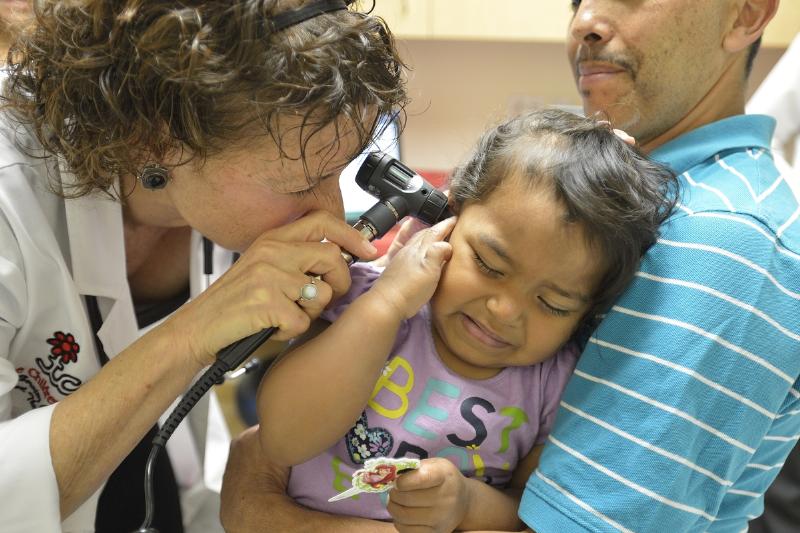Roy Vidal holds his daughter, Savannah Vidal, as Dr. Elisa Nicholas check her for an ear infection