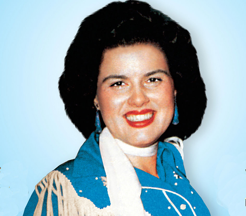 Patsy smiles in bright red lipstick and a bright blue outfit