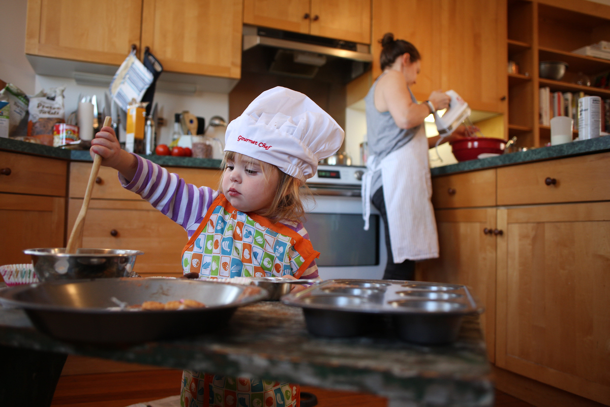A two year old girl cooking with her mum in the kitchen as mum prepares a bake mixture.
