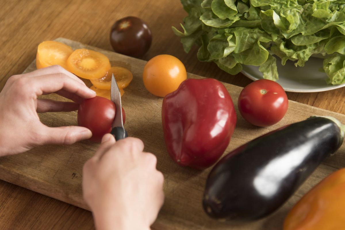 Young woman slicing vegetables on a wooden cutting board. 