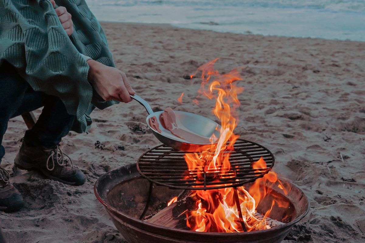 Camper cooks bacon over an open fire on the beach in Tynemouth, United Kingdom