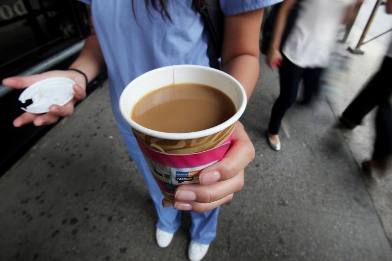 A woman holds a to-go cup of coffee on the street.