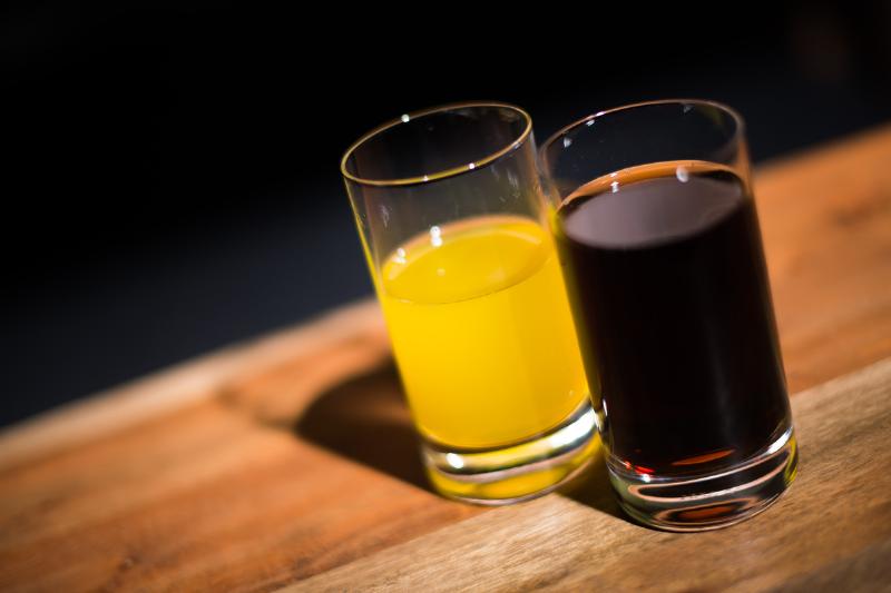 A glass of coca cola sits next to a glass of orange lemonade.