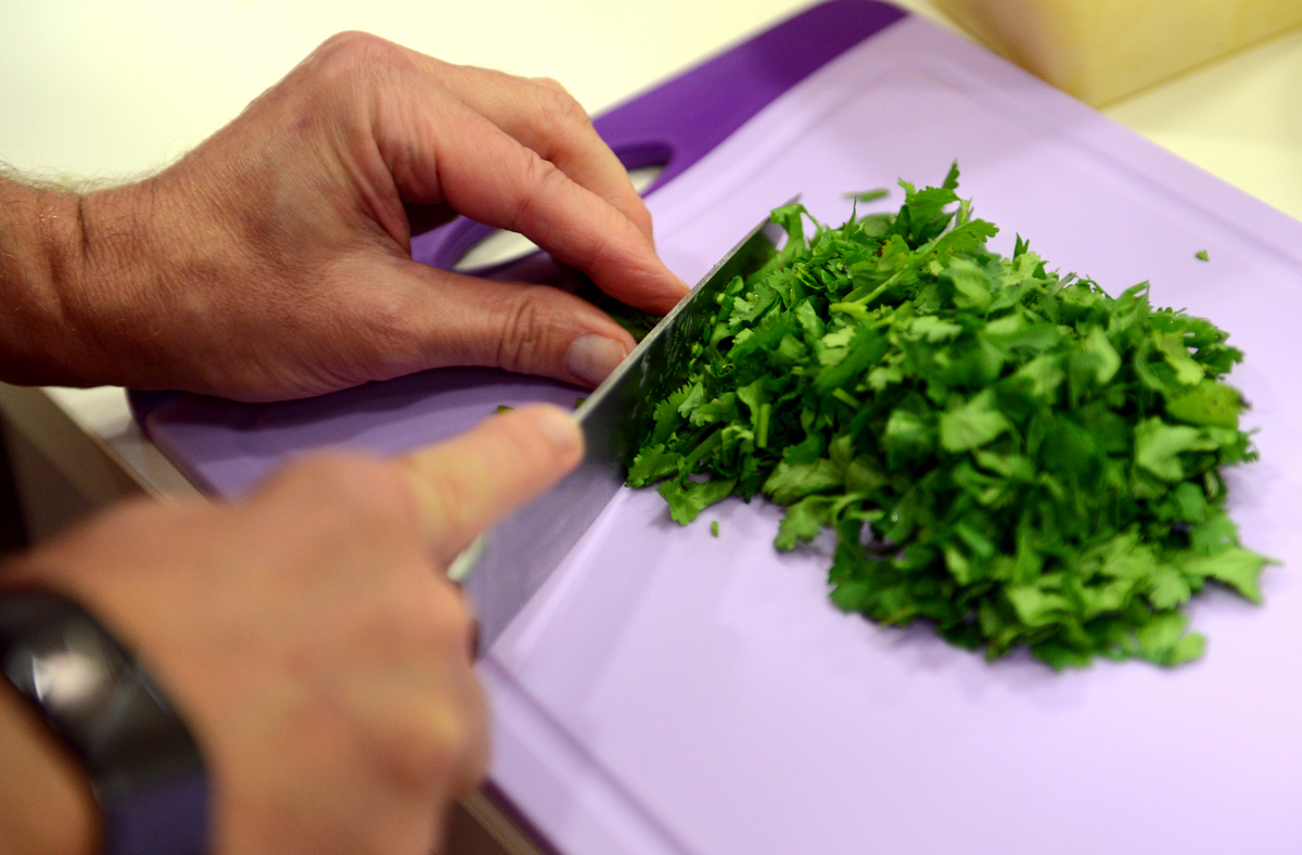 The blind employee Klaus Mueller chops parsley on a cutting board.