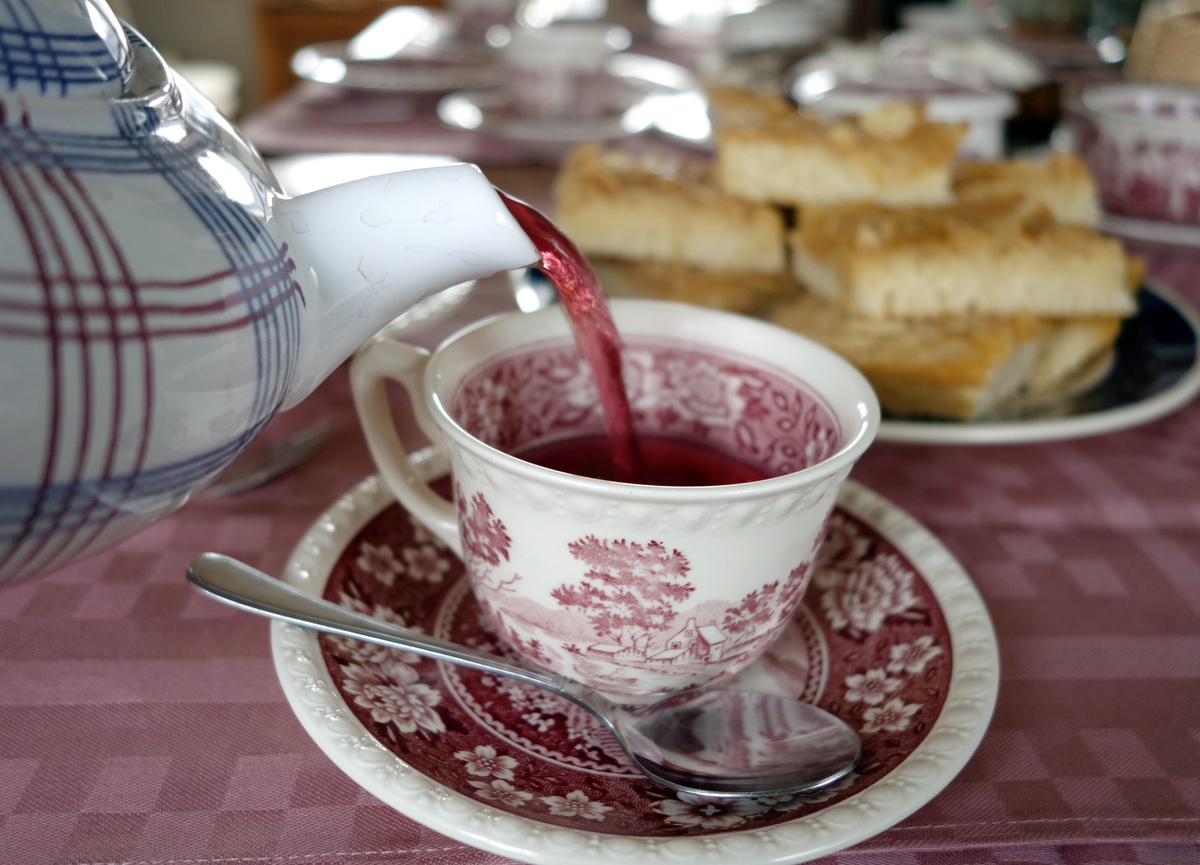 Tea pours out of a tea pot into a porcelain cup on a table.