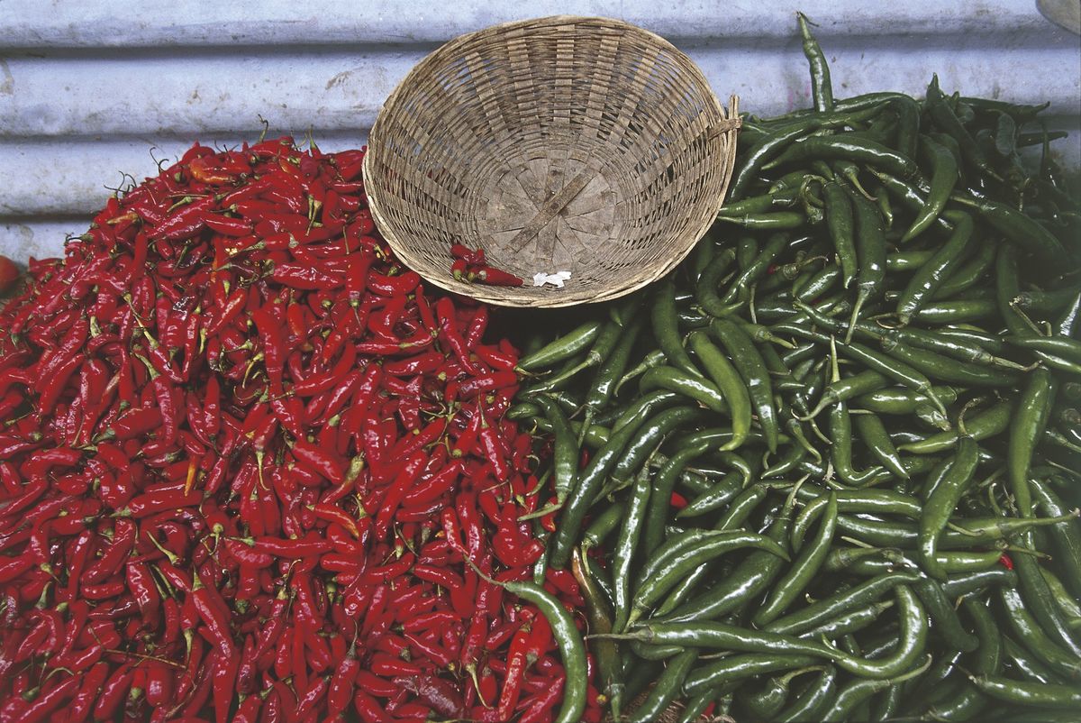 Red and green chili peppers line up near a woven basket.