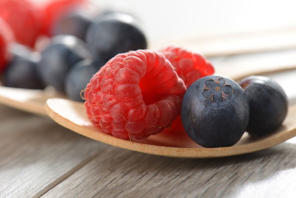 A small wooden plate holds raspberries and blueberries.