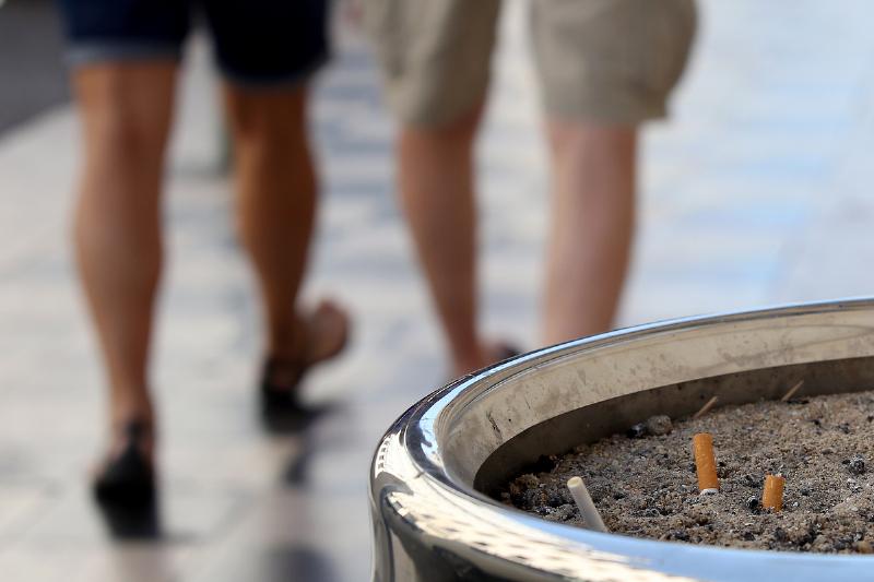 Two people walk away from an ashtray. 