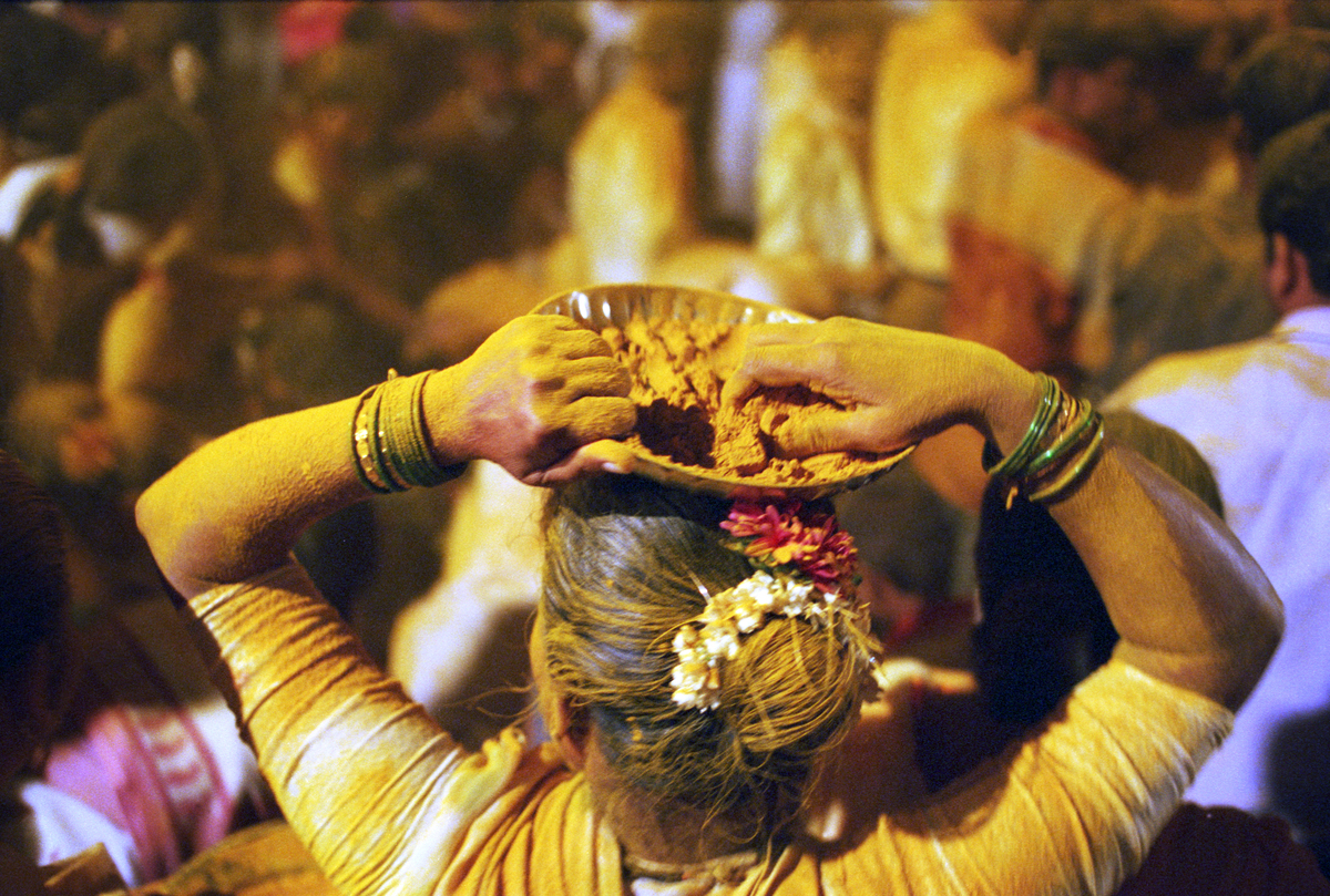 Woman at a Hindu festival throws powdered yellow turmeric and chunks of coconut over revellers from a basket on her head.