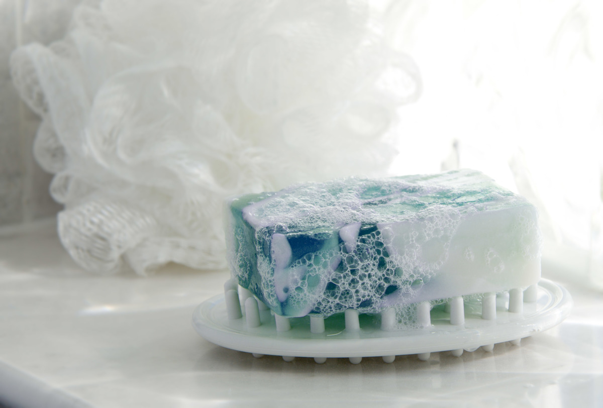 A bar of glycerin soap rests on a soap dish in front of a loofah.