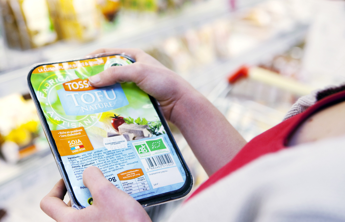 Woman holds and examines tofu at an organic supermarket.