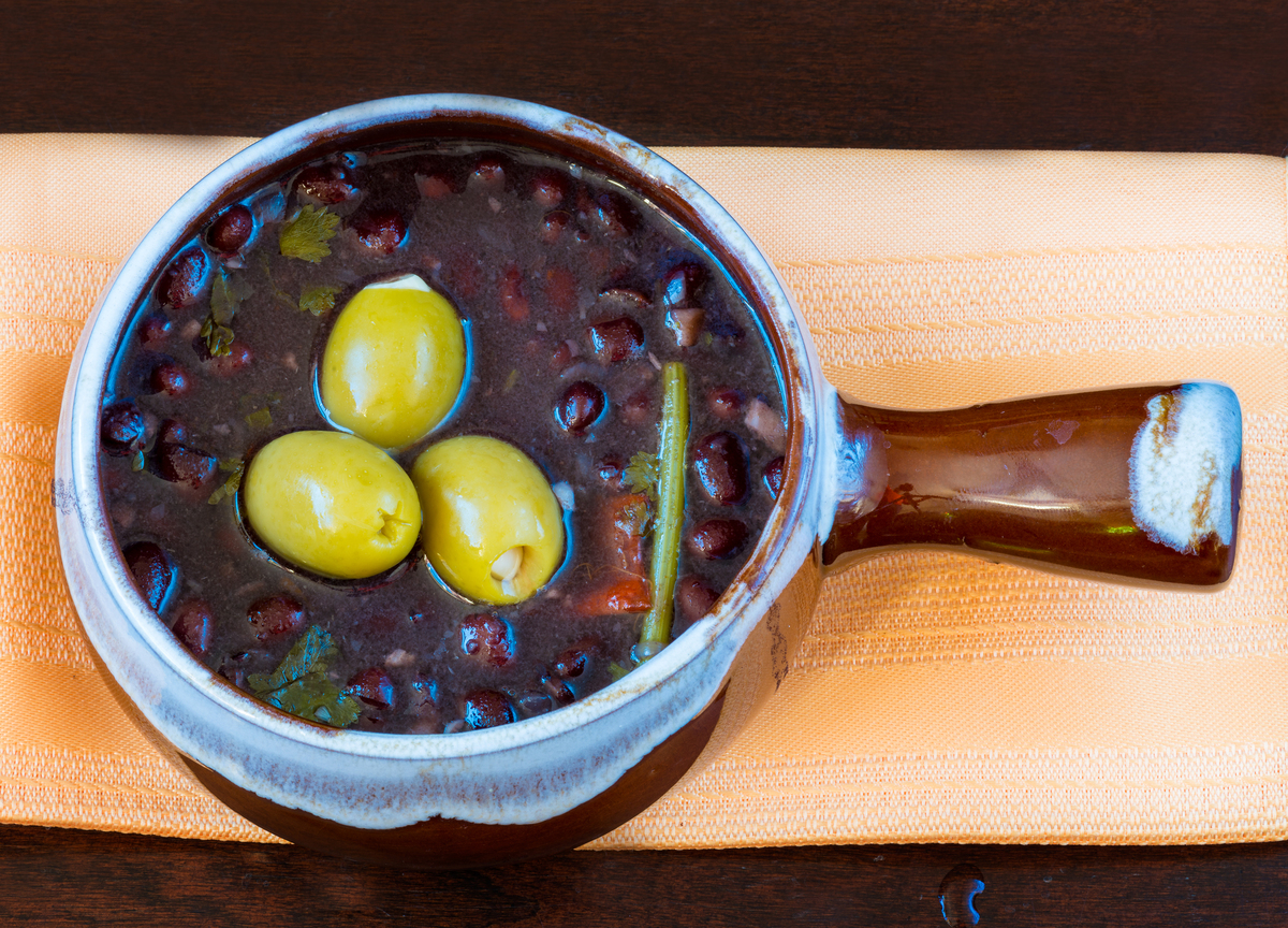 A clay pot filled with black bean soup rests on a towel.