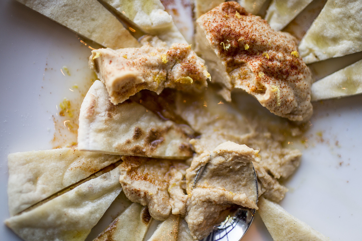 Pita and bread are dipped into a pile of hummus.