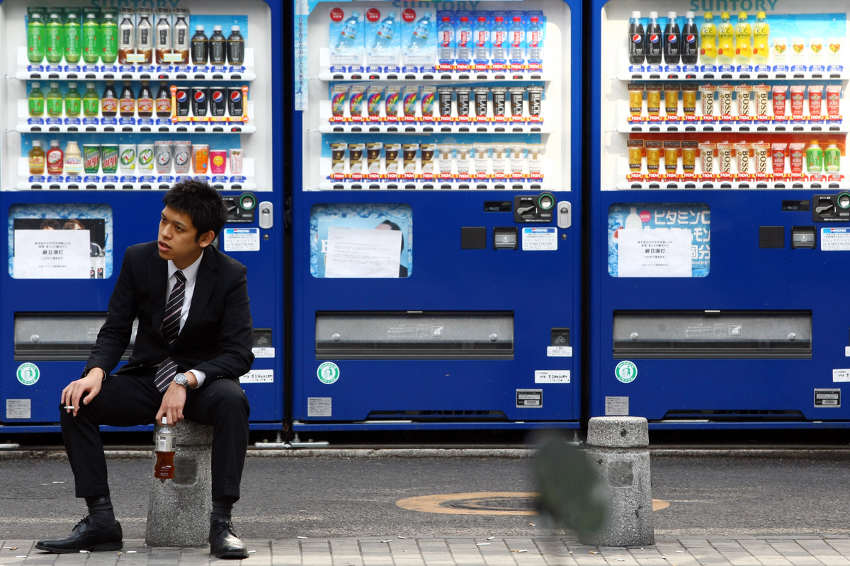 Man sits and drinks a soda that he bought from a vending machine.