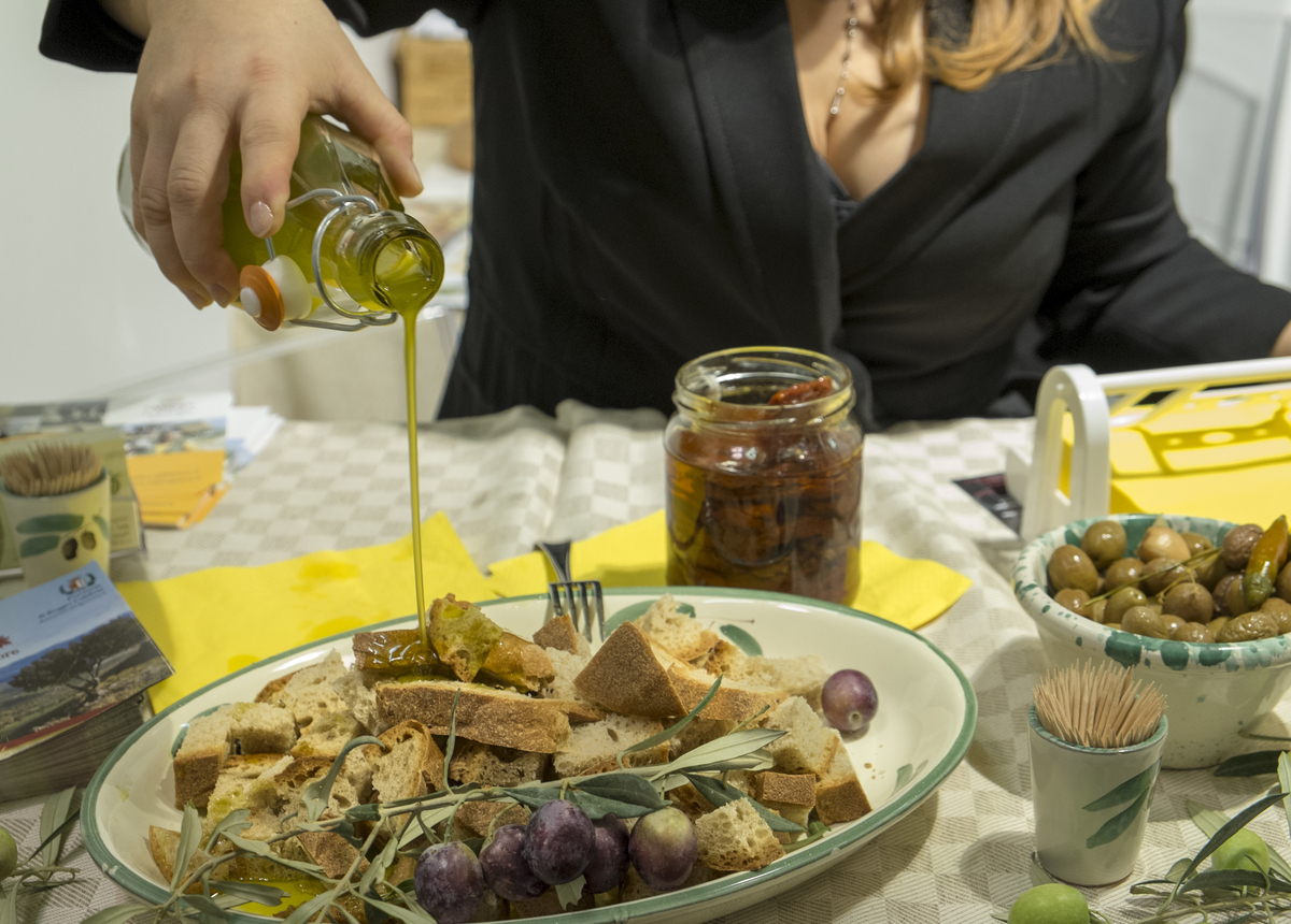 A woman pours Olive Oil over some bread.