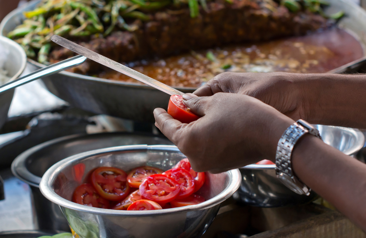 Man slices tomatoes over a silver bowl.