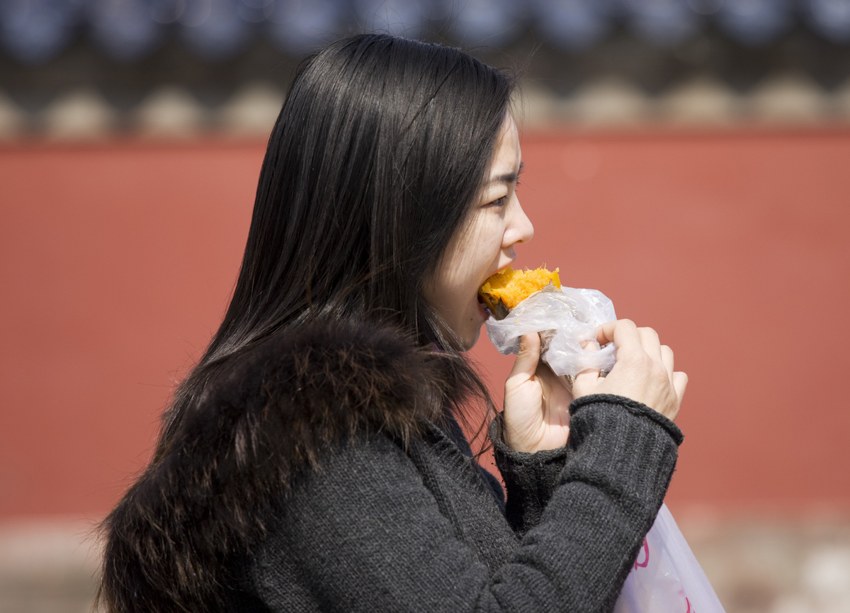 Girl eats a sweet potato at the Ming Dynasty Temple of Heaven, Beijing, China.
