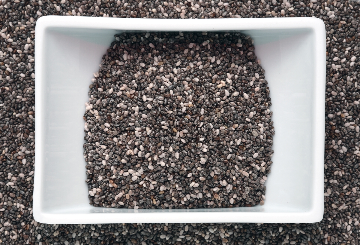 A sqaure-shaped bowl of chia seeds rests on more chia seeds.