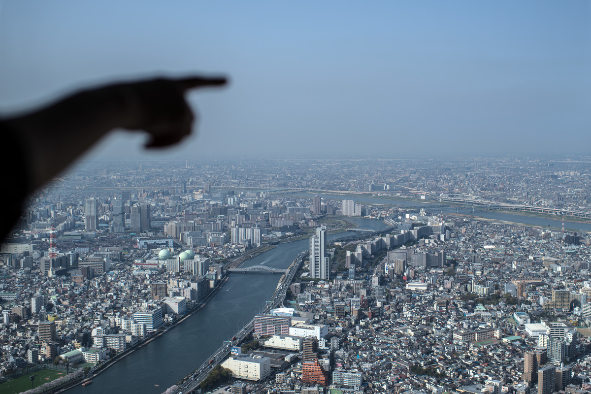 A woman points towards the Tokyo skyline from the viewing platform of the Tokyo Skytree.
