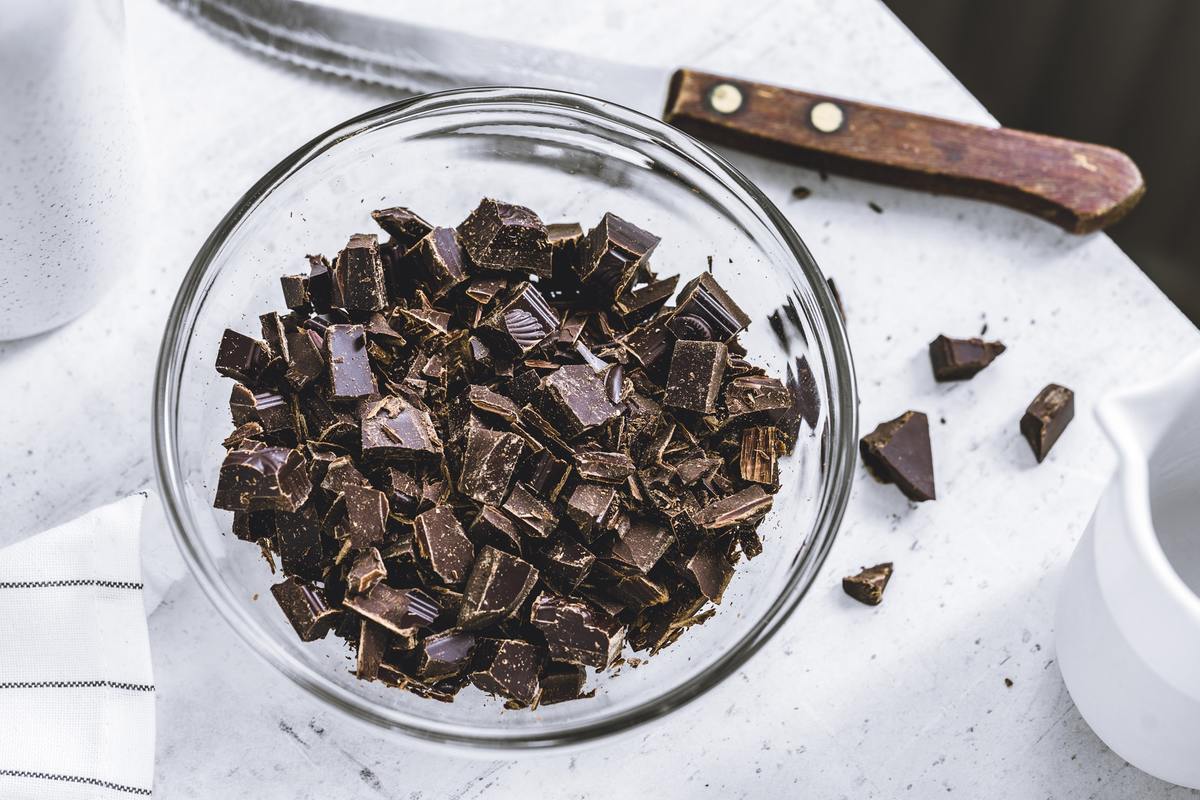 Chopped dark chocolate is gathered in a glass bowl.
