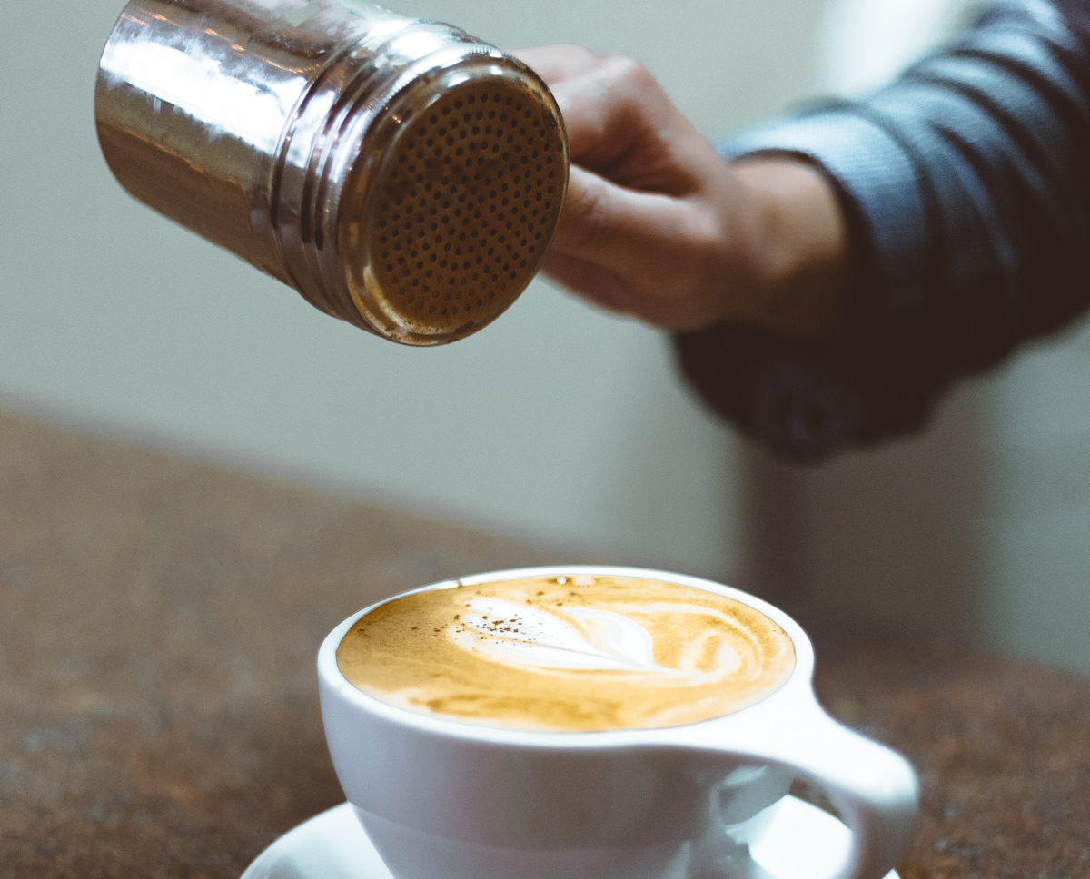 Man sprinkles some cinnamon on a latte.