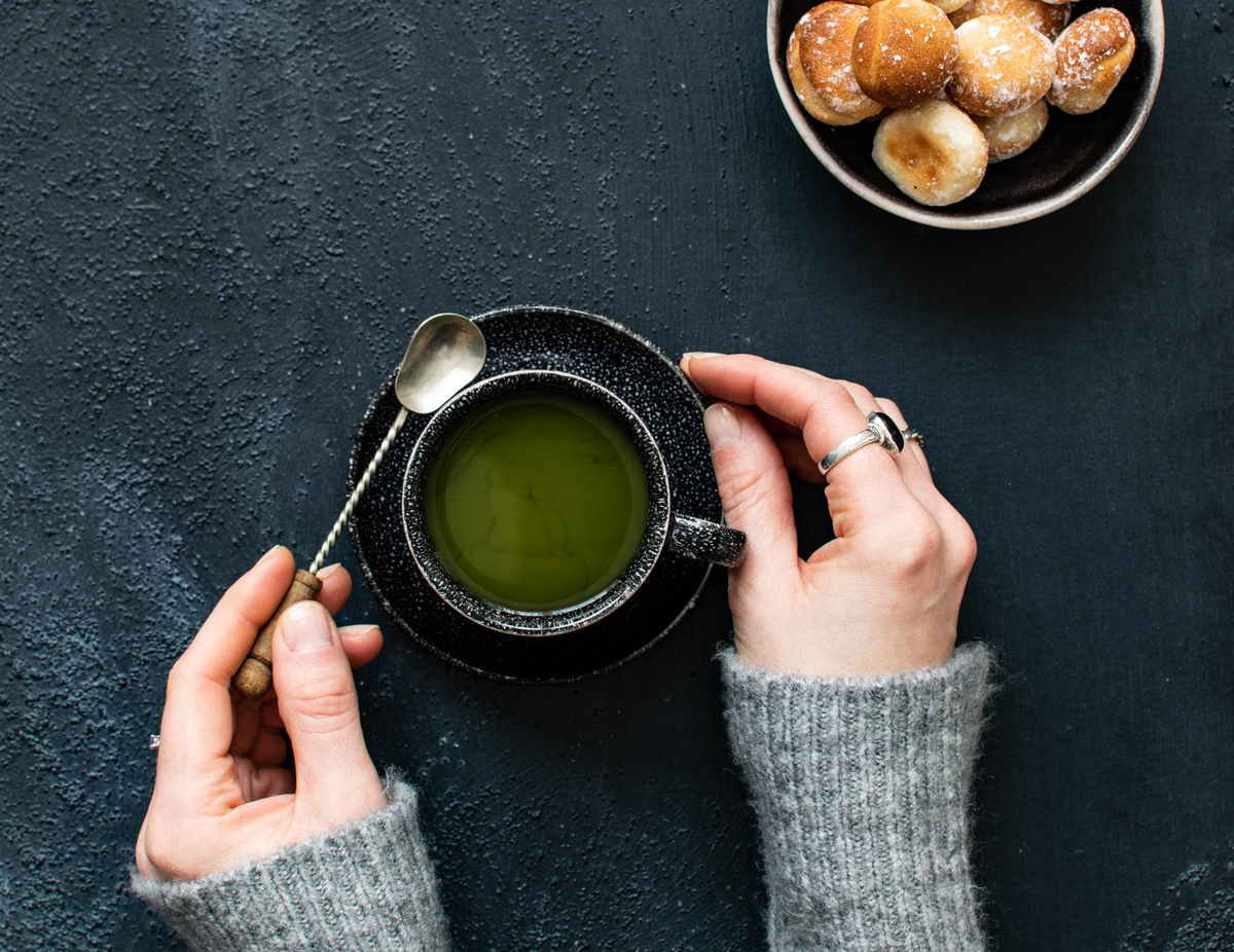 A woman lifts a spoon out of a cup of green tea.