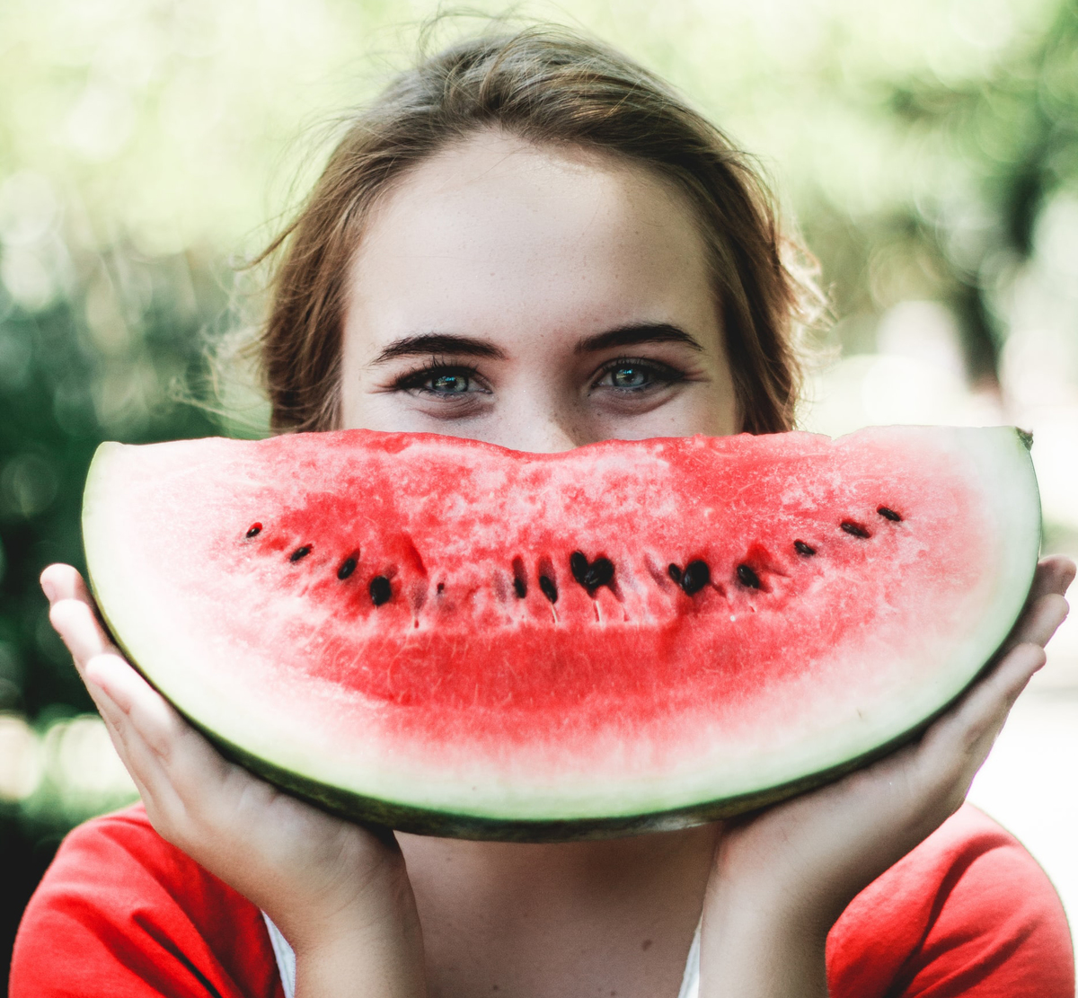 Woman holds a large slice of watermelon in front of her face.