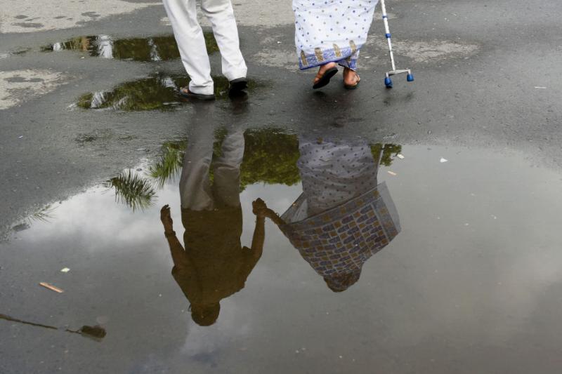 An elderly couple holds hands while crossing a wet street.
