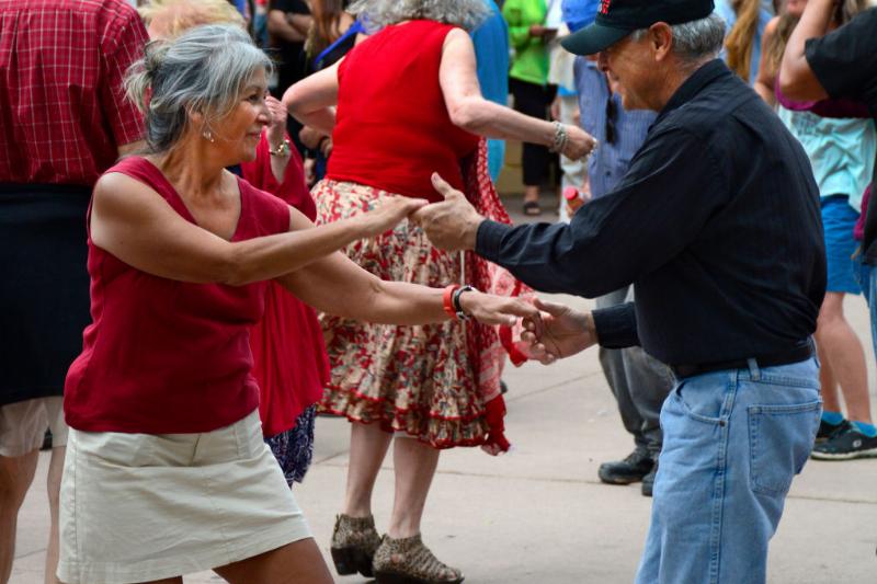 A retired couple dancing outside amongst a crowd.