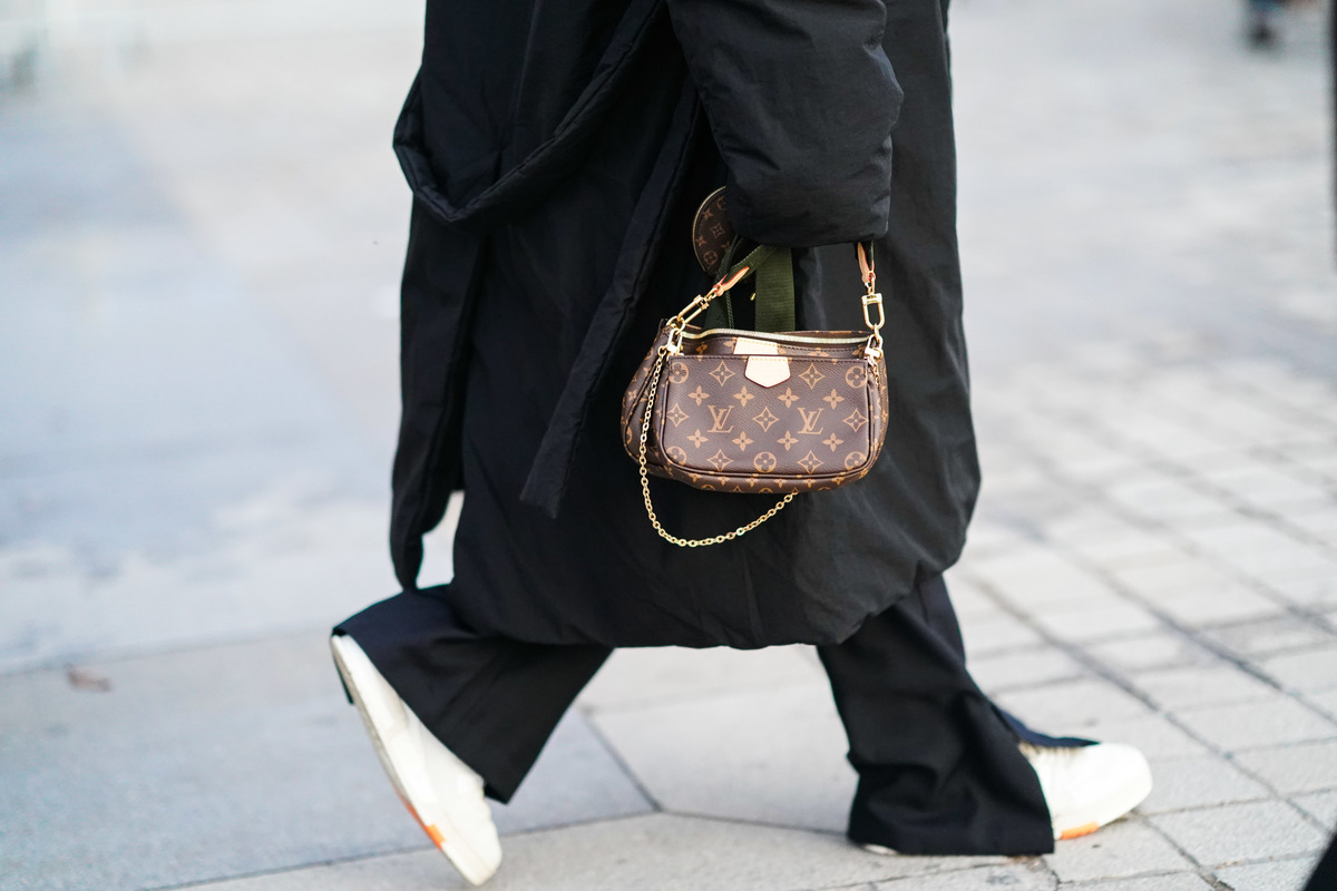 A person wearing an oversized coat carries a small Louis Vuitton bag.