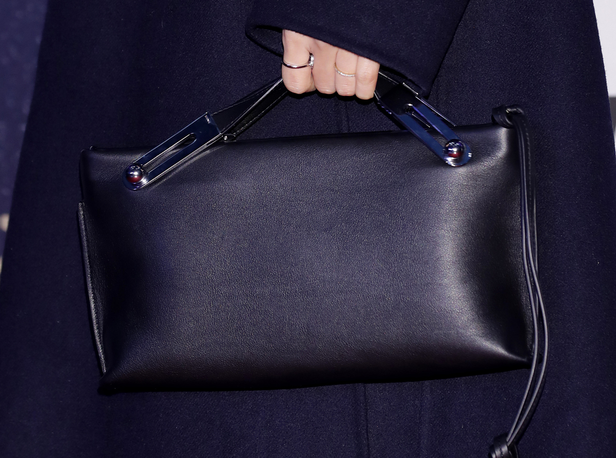 A woman holds a plain black rectangular purse.