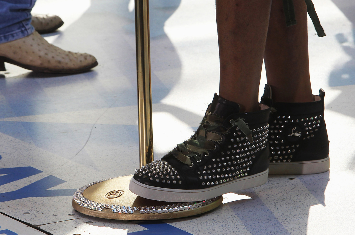 A person with bedazzled shoes steps on a microphone stand.