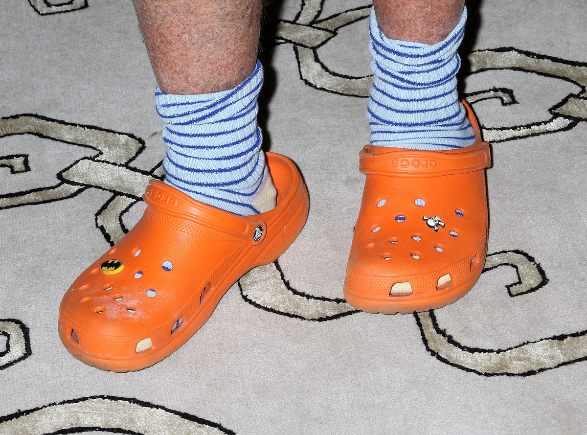 A man wears orange crocs with skull and Batman decorations.