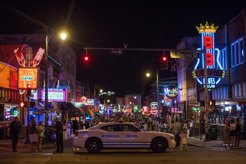 a shot of beale street lit up at night with a police car and crowd of people