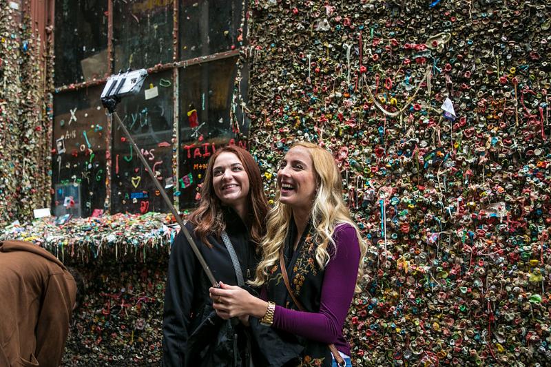 two girls taking a selfie in front of a gum wall