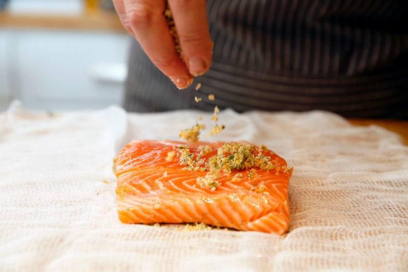 someone sprinkling bread crumbs on a piece of raw salmon
