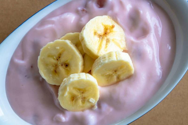 Fruit-flavored yogurt is served in a bowl with sliced banana on top.