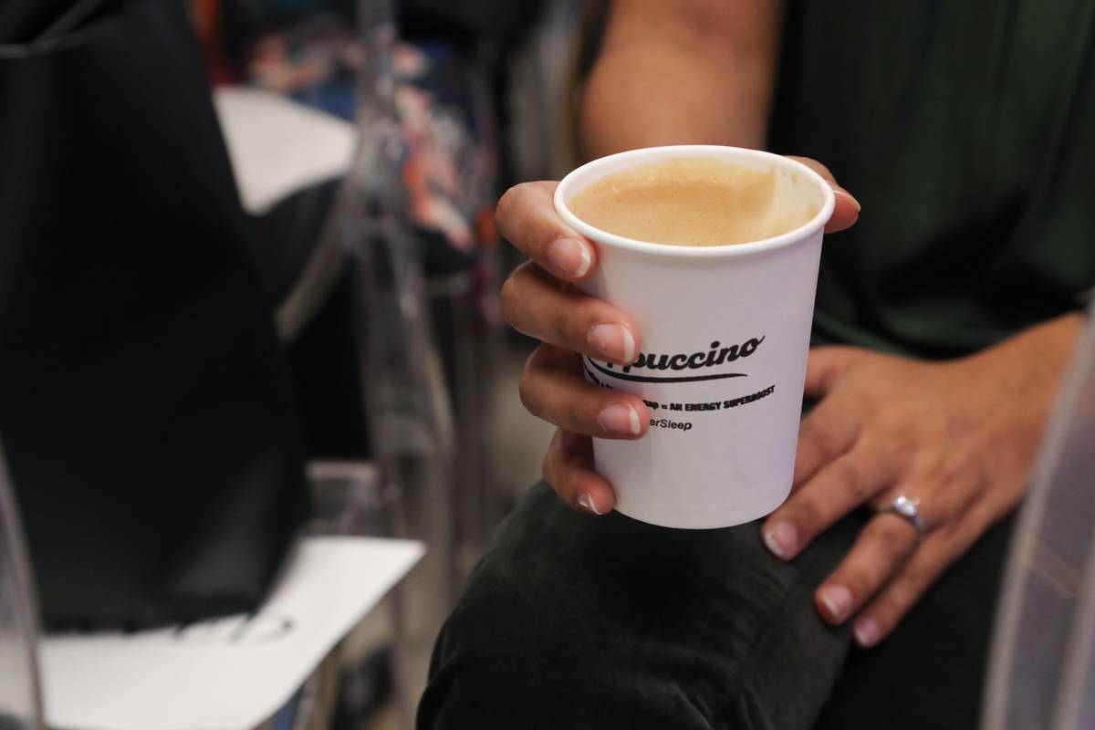 A woman holds a to-go cup of cappuccino.