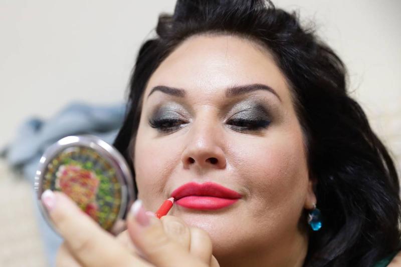A beauty pageant model applies lipstick.