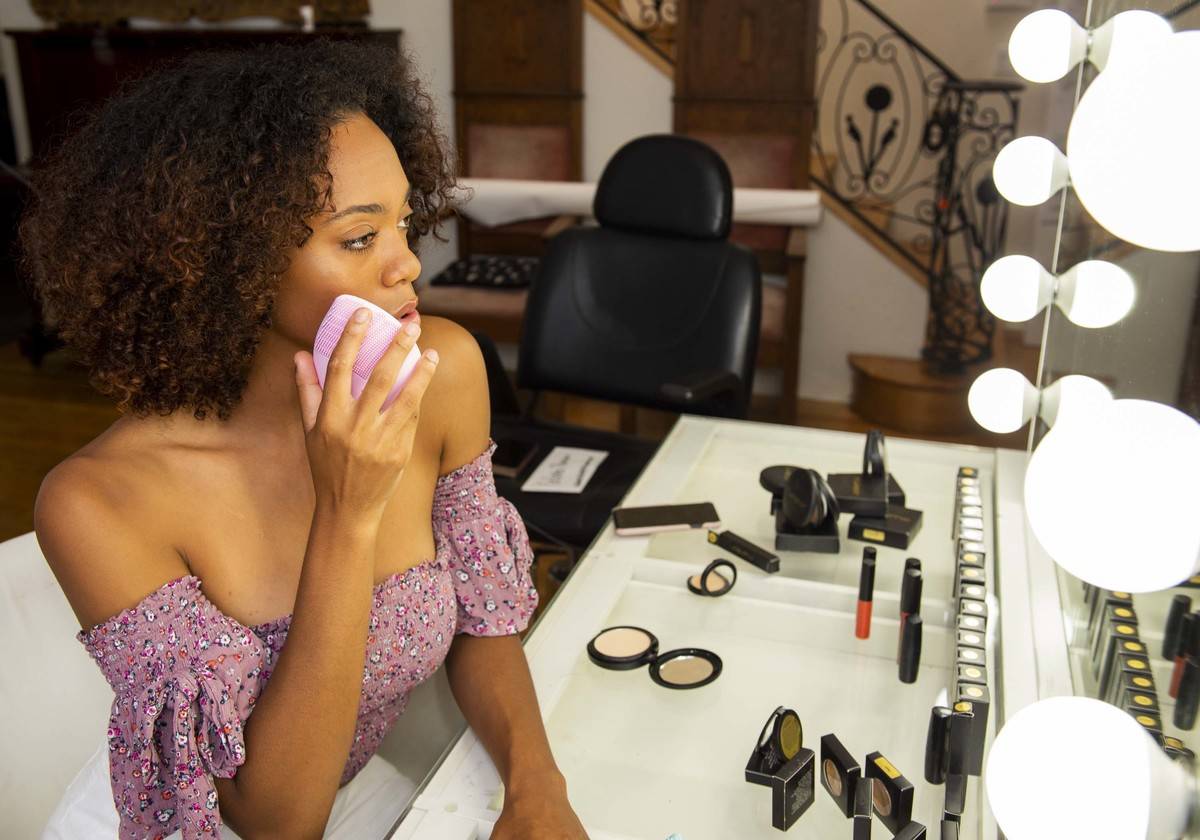 A woman uses a skincare device to remove makeup.