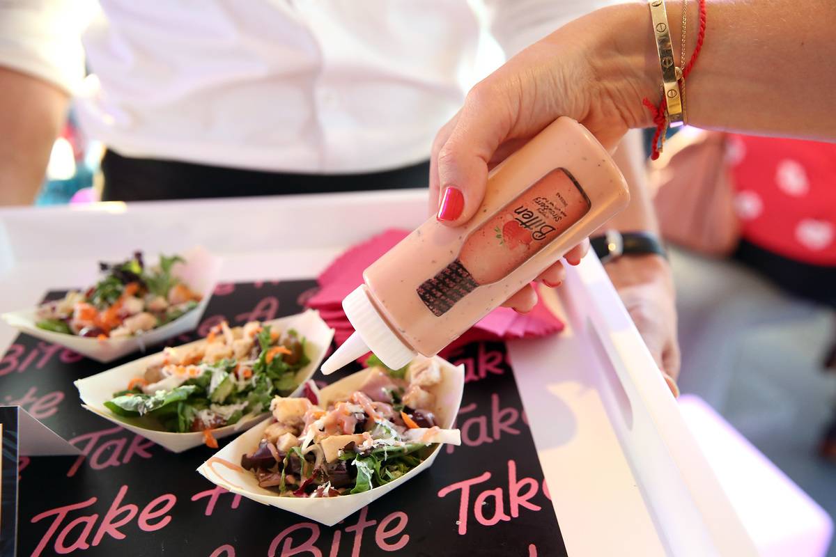 A woman pours salad dressing from a bottle onto a salad.