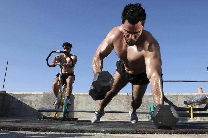Two bodybuilders work out outside.